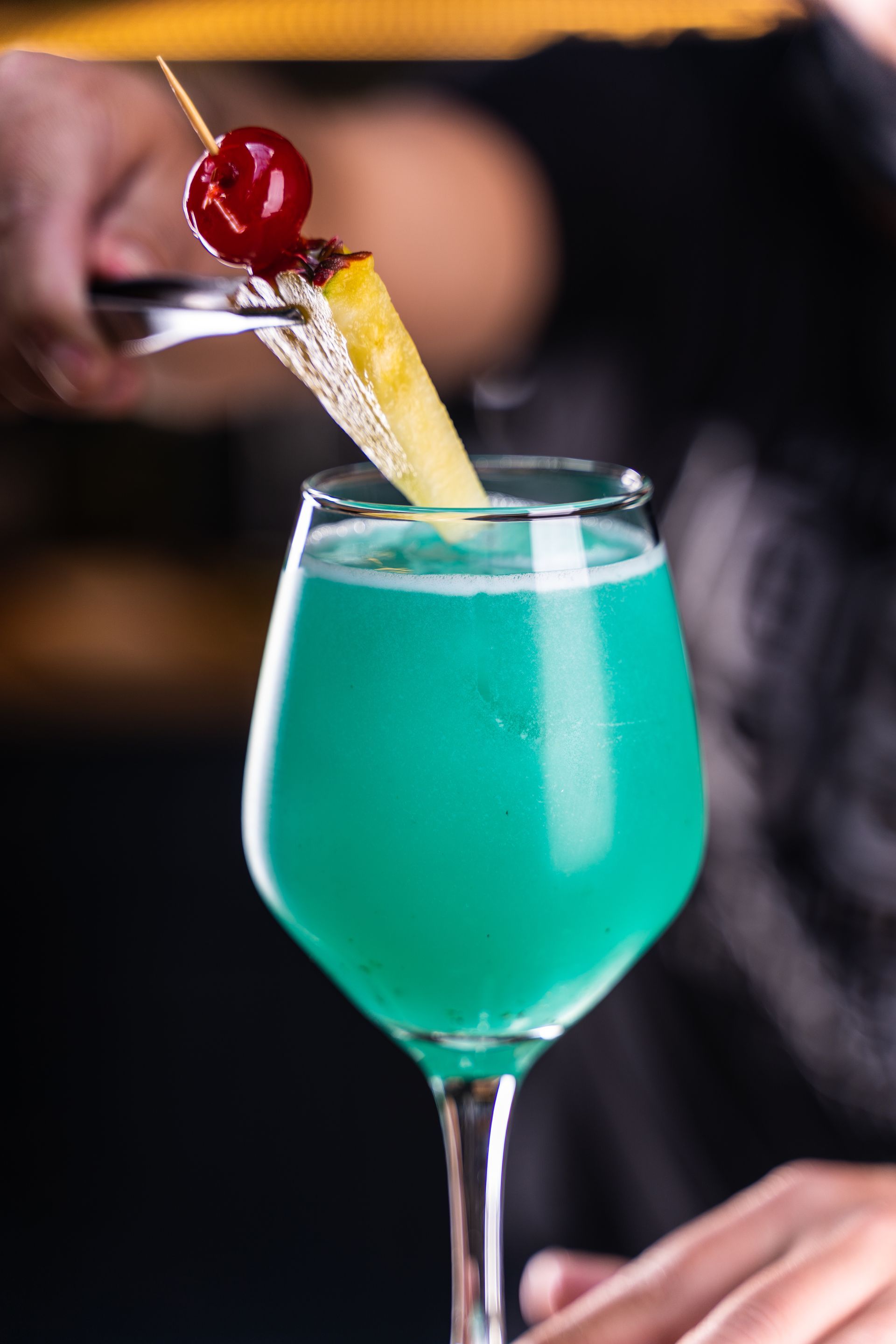 Cocktail turquoise servi dans un verre à pied, garni d'un quartier d'ananas et d'une cerise, présenté au bar.