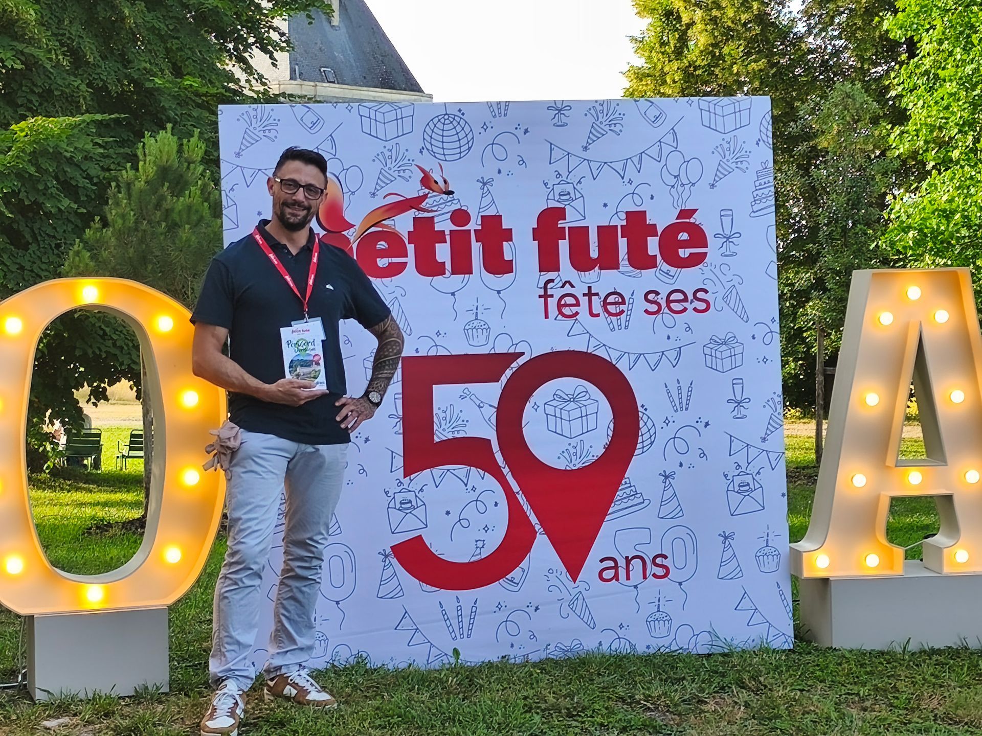 Un homme pose à côté d'une enseigne Petit Futé fête ses 50 ans en extérieur.