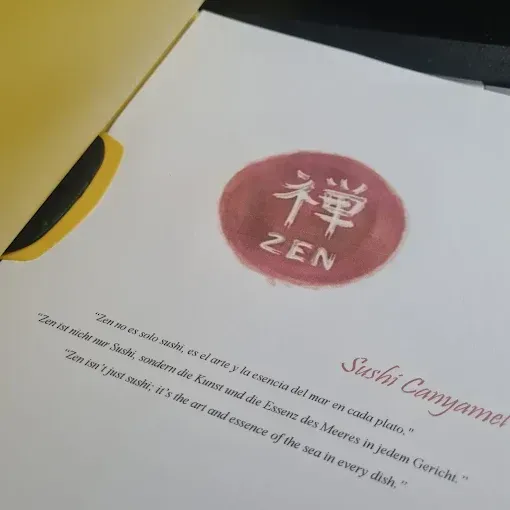 Tarjeta blanca con el logotipo “ZEN” en rojo y caligrafía dorada en la superficie, con un texto cursivo tenue debajo.