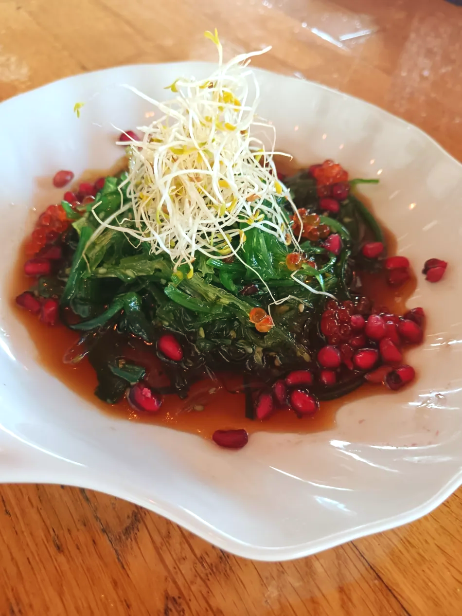 Ensalada gourmet en plato blanco con hojas verdes, semillas de granada roja y guarnición rallada.