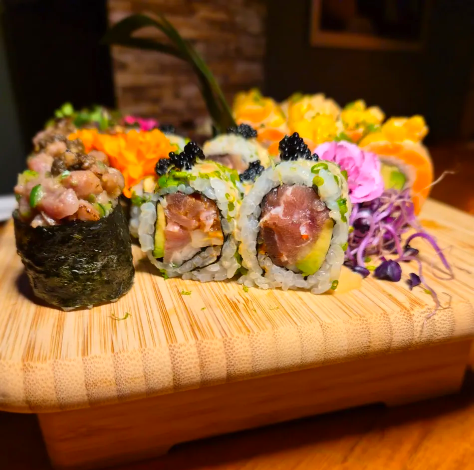 Rollos de sushi en una tabla de madera con guarnición colorida y col morada, presentación de restaurante en primer plano.
