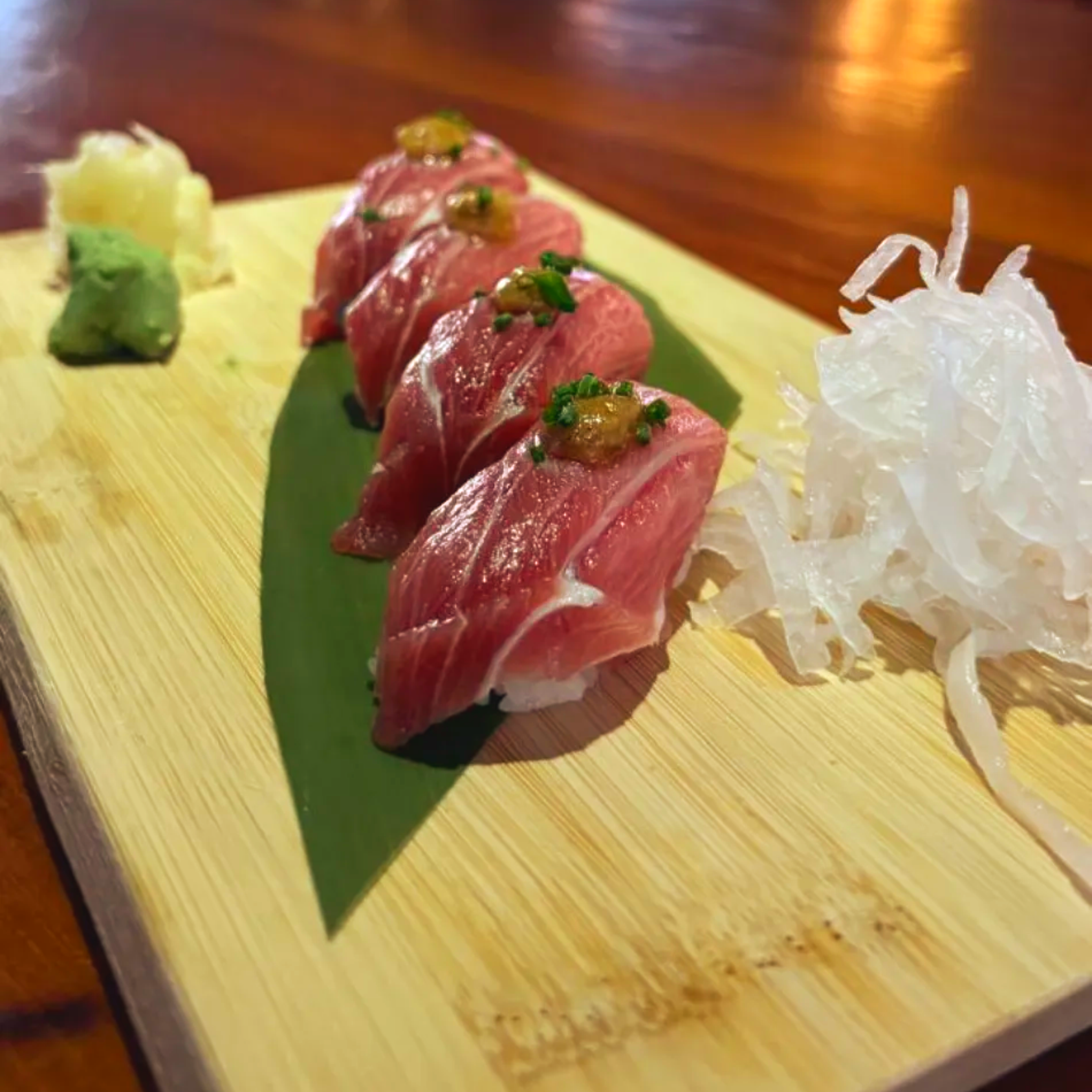 Sashimi de atún en rodajas sobre una tabla de madera con wasabi, jengibre y rábano daikon rallado como guarnición.