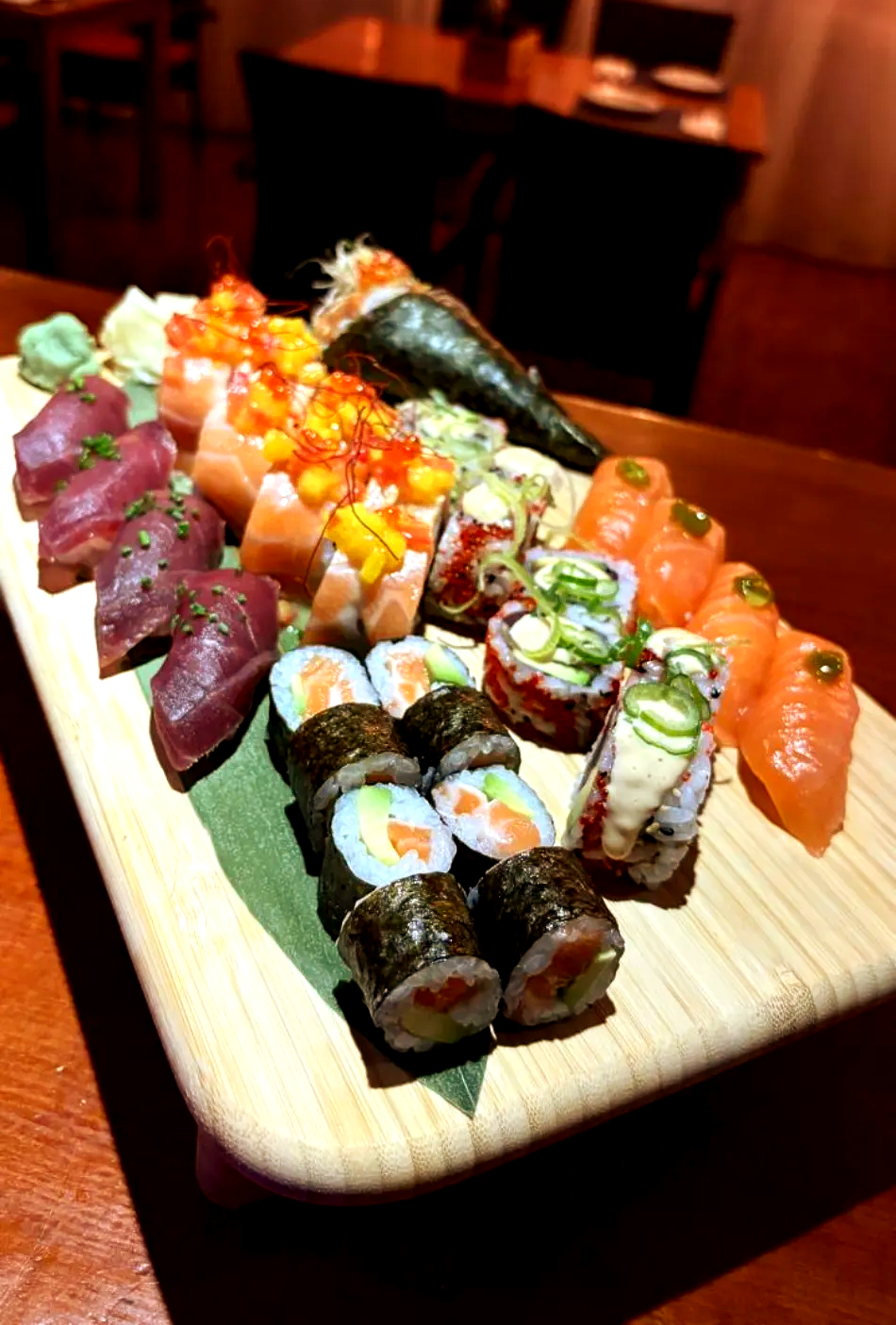 Surtido de rollos de sushi y sashimi en una bandeja de madera en un restaurante con luz tenue.
