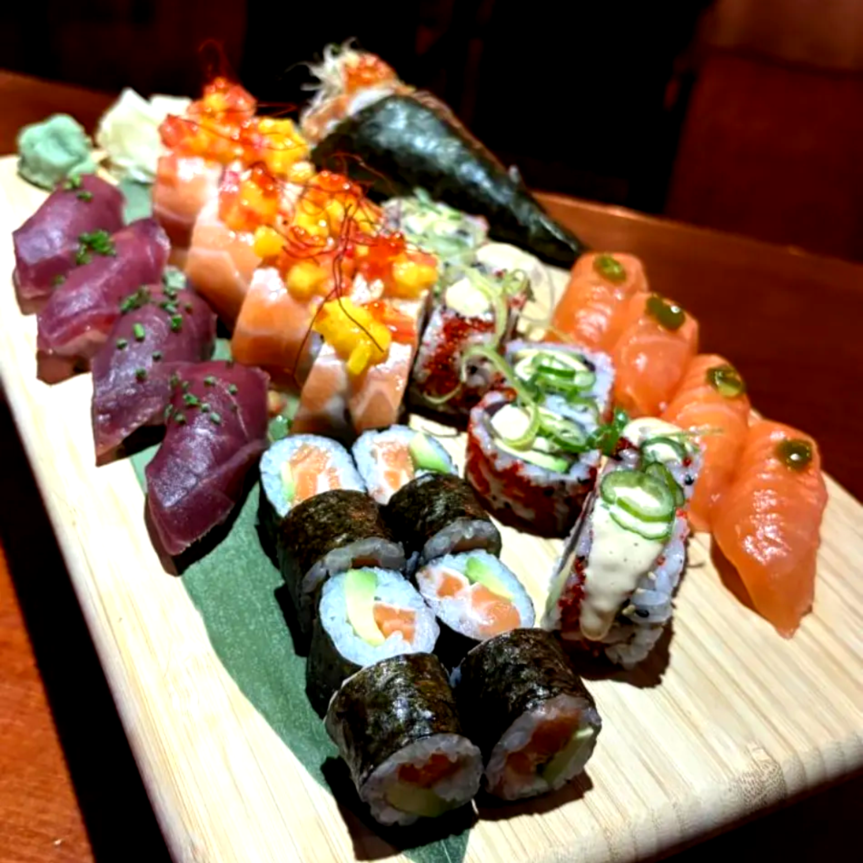 Surtido de rollos de sushi y nigiri dispuestos en una bandeja rectangular, con aderezos de salmón, atún y huevas.