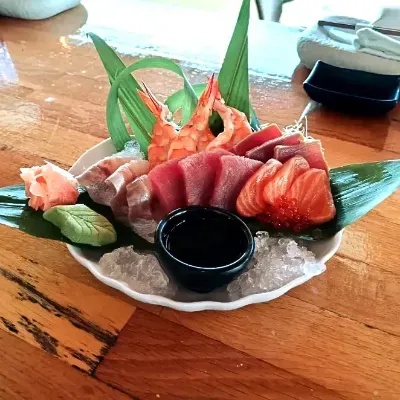 Plato de sashimi con salmón, atún, camarones, wasabi y salsa de soja en un plato forrado con hojas.