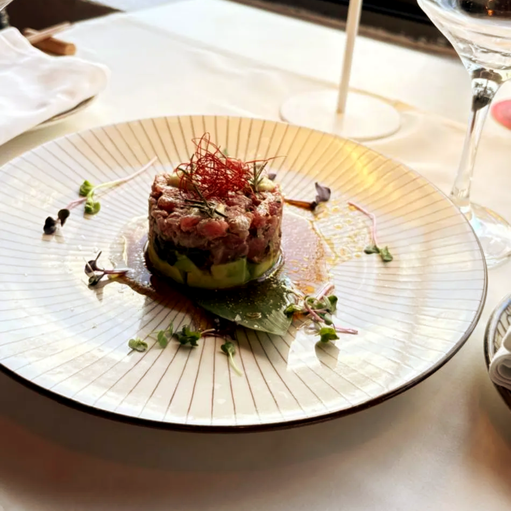 Aperitivo gourmet presentado con guarnición roja en un plato blanco en un ambiente elegante y con iluminación tenue.