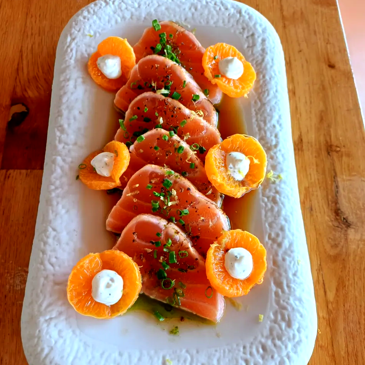 Salmón en rodajas y rodajas de naranja adornadas con hierbas en un plato rectangular blanco.