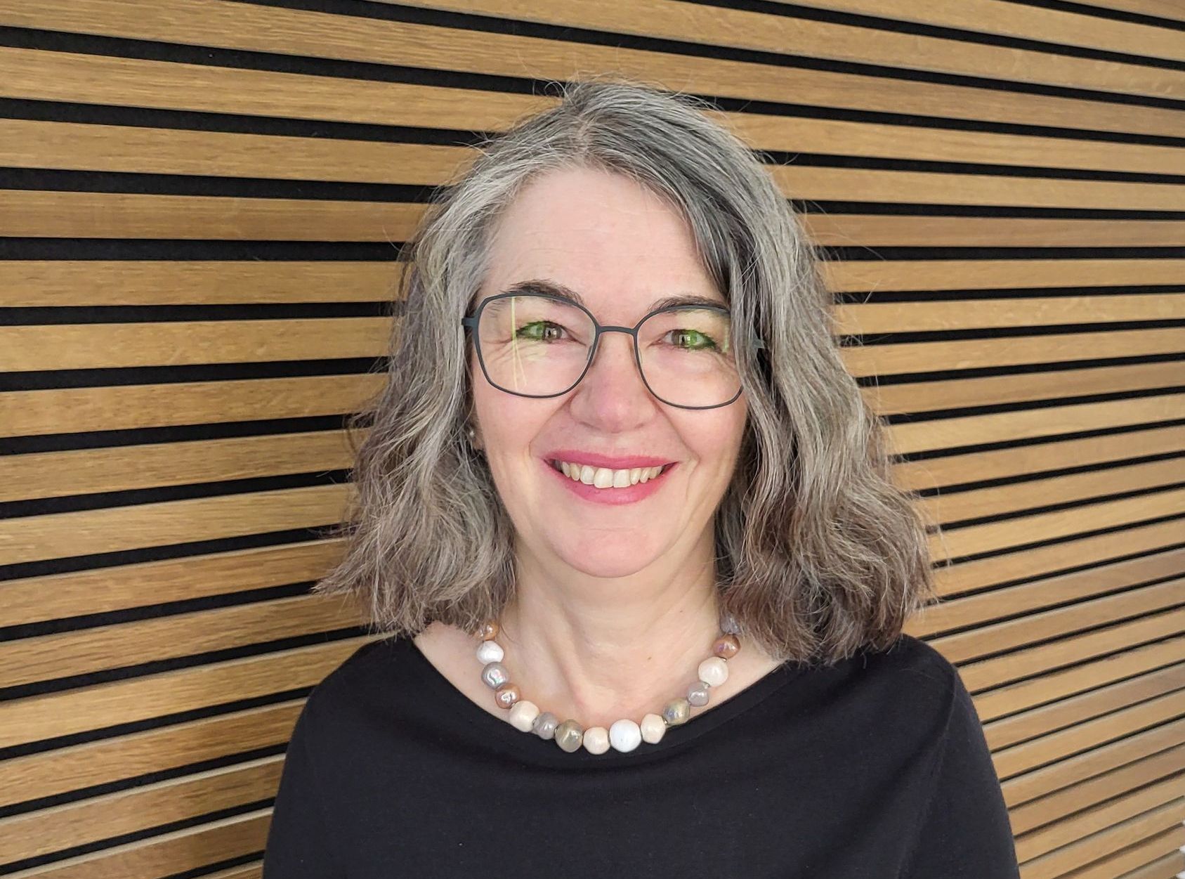 Eine Frau mit Schal und gestreiftem Pullover lächelt in die Kamera.