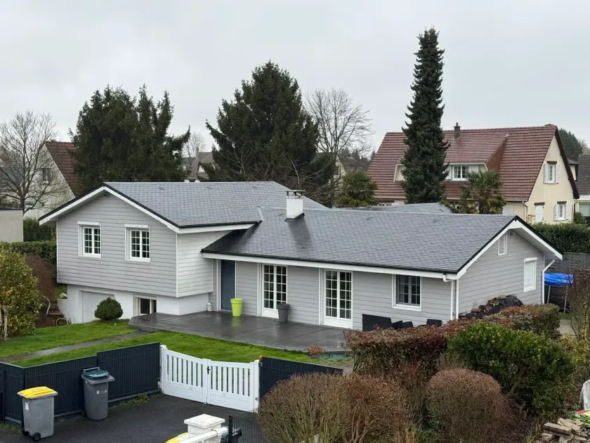 Maison de banlieue grise de plain-pied avec des boiseries blanches et un toit foncé, vue depuis la rue.