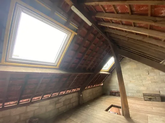 Intérieur des combles avec toit en pente, briques apparentes, poutres en bois et puits de lumière éclairant le sol