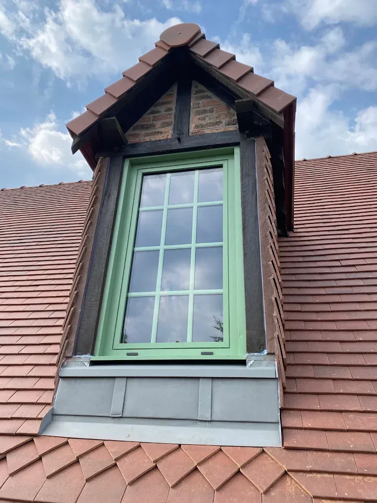 Lucarne à cadre vert, toit en bardeaux bruns et ciel nuageux au-dessus