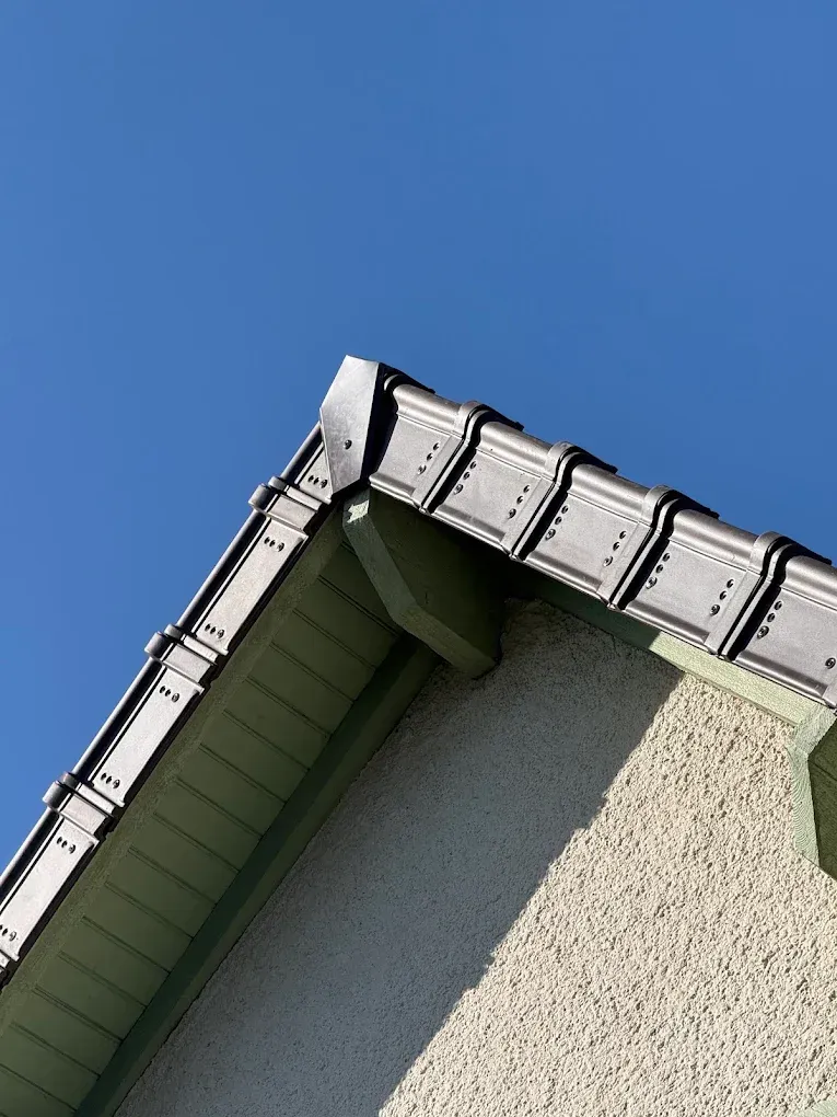 Coin de toit de maison avec gouttières blanches sur un ciel bleu clair
