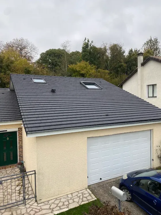 Maison de banlieue avec toit gris, porte de garage blanche et voiture bleue garée devant