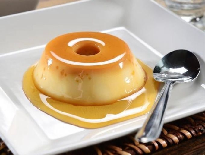 Flan de caramelo en un plato blanco con una cuchara al lado.