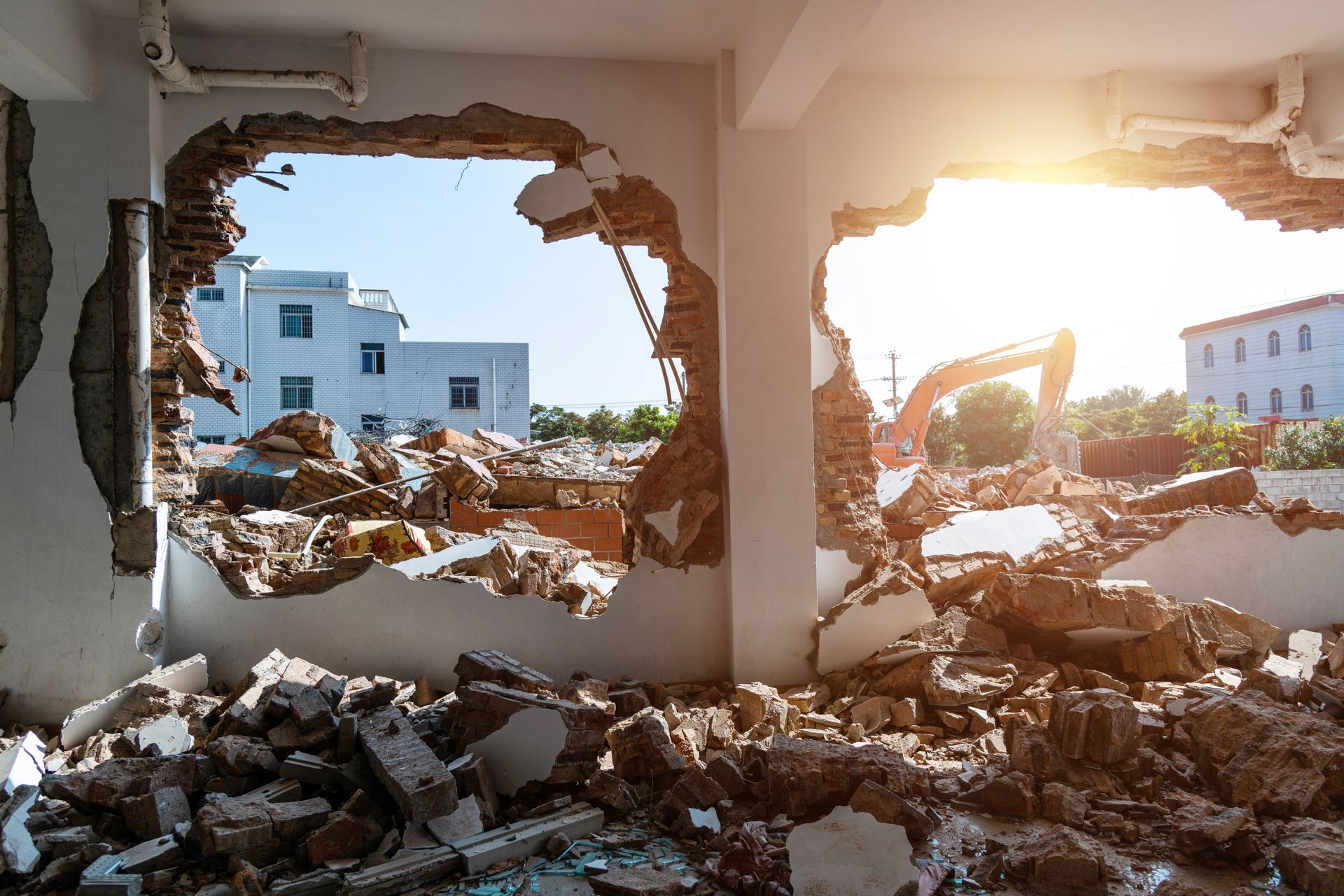 Photo d'un mur blanc en cours de démolition, un tas de gravats en arrière-plan vu à travers un des deux trous percés dans le mur.