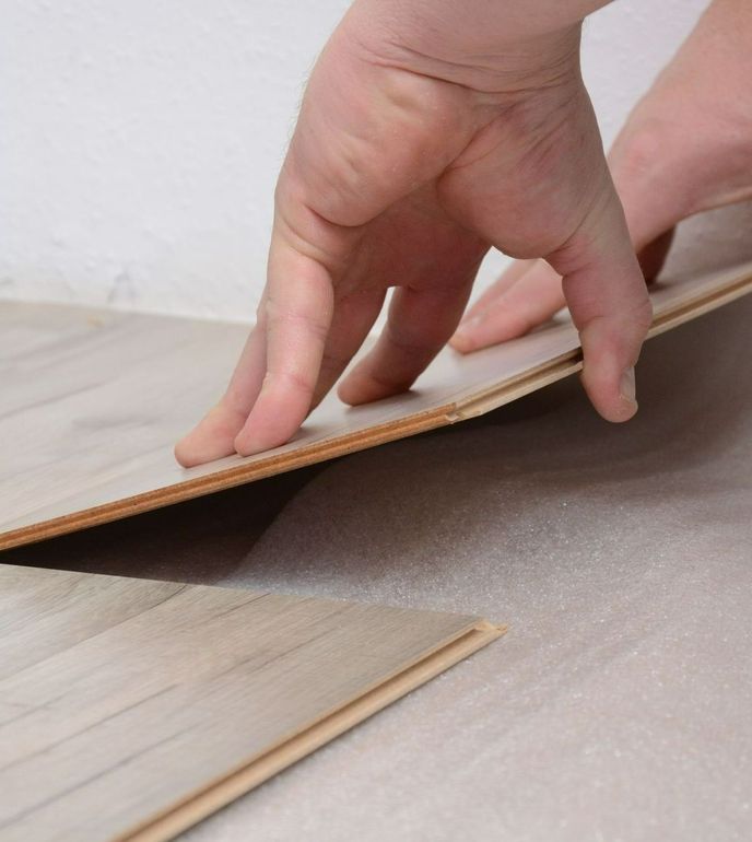 Photo de deux mains vues de biais, en train de poser ou de déposer un plancher en bois
