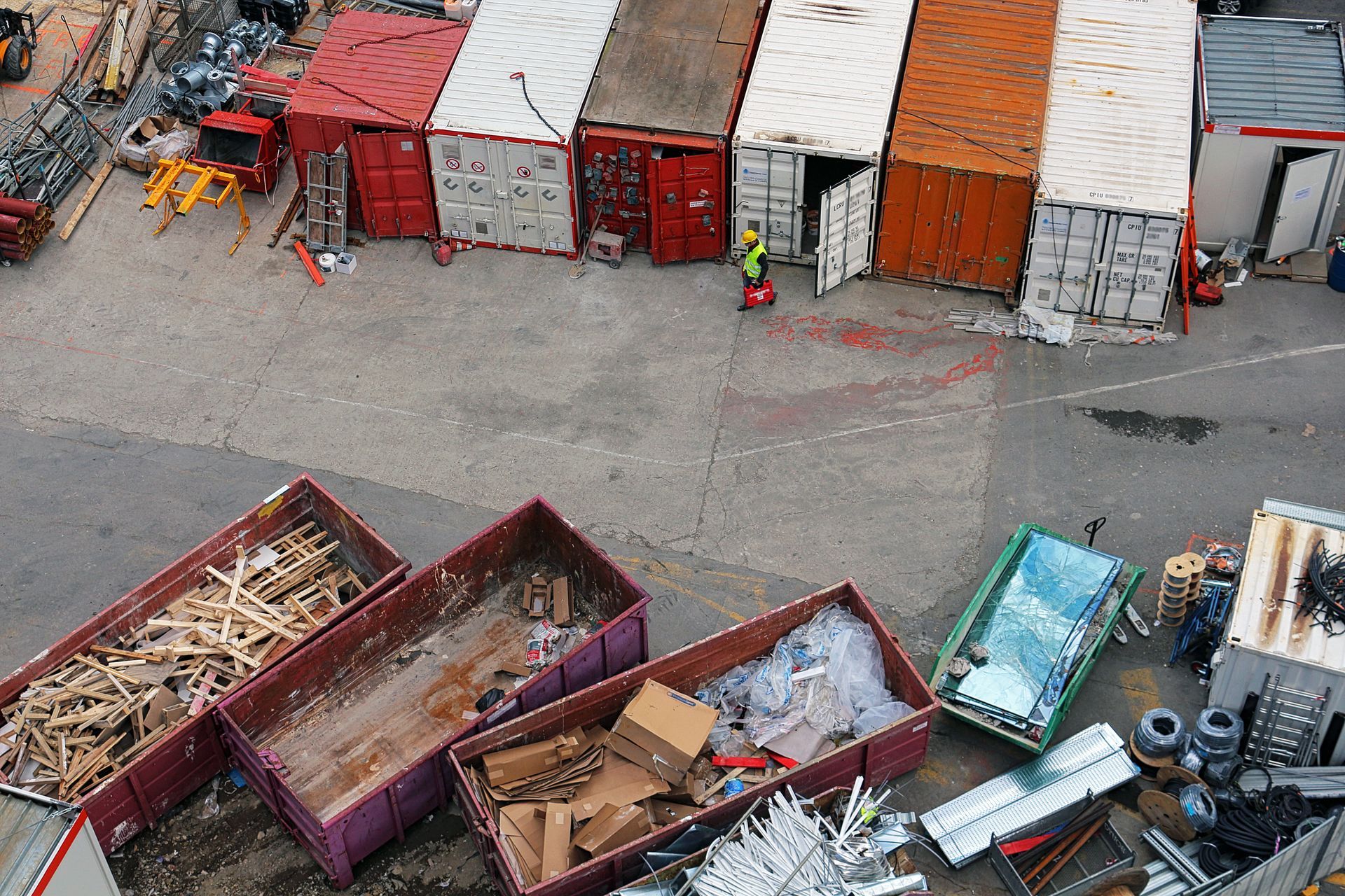 Photo d'un camion benne jaune vu de trois quarts qui dépose des déchets sur un tas de gravats. À l'arrière-plan, des bâtiments et un tas de terre.