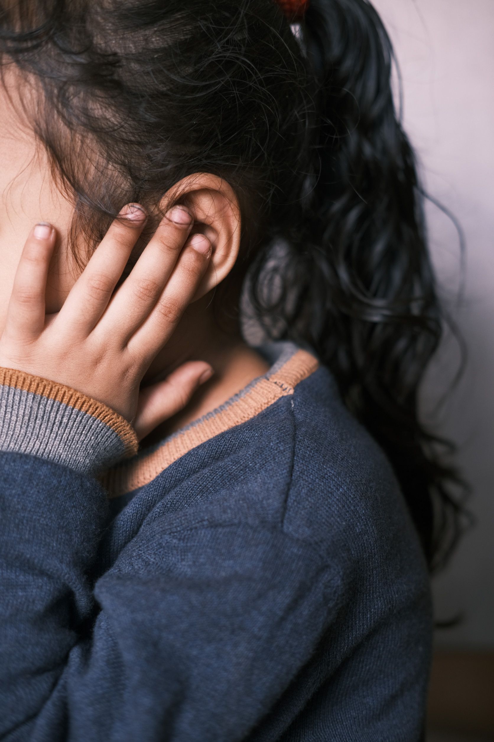 Una niña se cubre la cara con las manos mientras viste un suéter azul.
