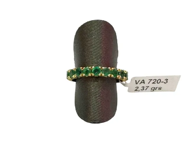 Anillo de oro con una banda de gemas verdes, sobre un soporte verde oscuro. La etiqueta indica