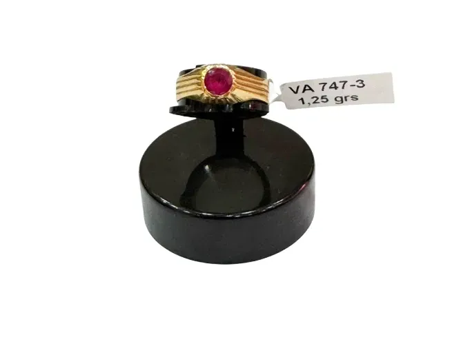 Anillo de oro con piedra roja sobre expositor negro, con etiqueta que dice