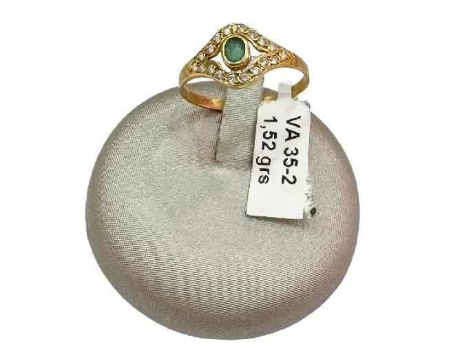 Anillo de oro con una esmeralda y pequeños diamantes, en un expositor gris. La etiqueta indica