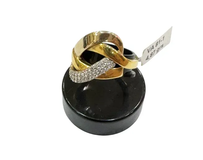 Anillo de oro y diamantes, diseño entrelazado sobre soporte de exhibición negro.