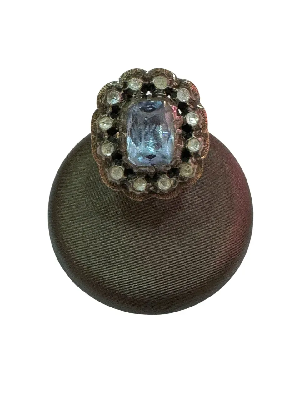 Un botón vintage con una gema azul claro rodeada de pequeñas piedras blancas. El botón es oscuro y texturizado.