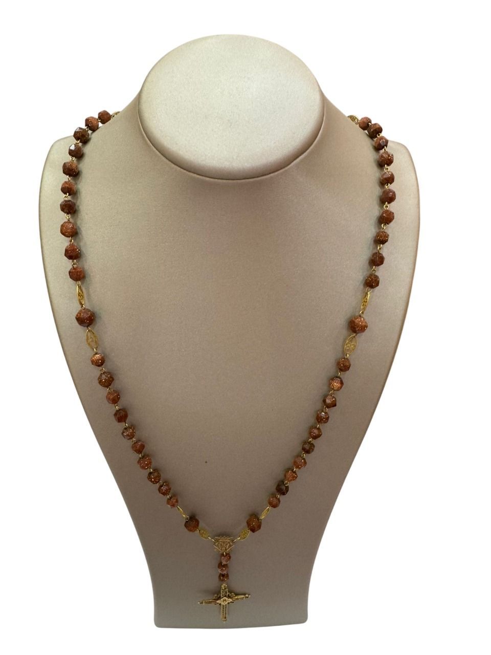 Collar con cuentas marrones y colgante de cruz dorada expuesto sobre un maniquí.