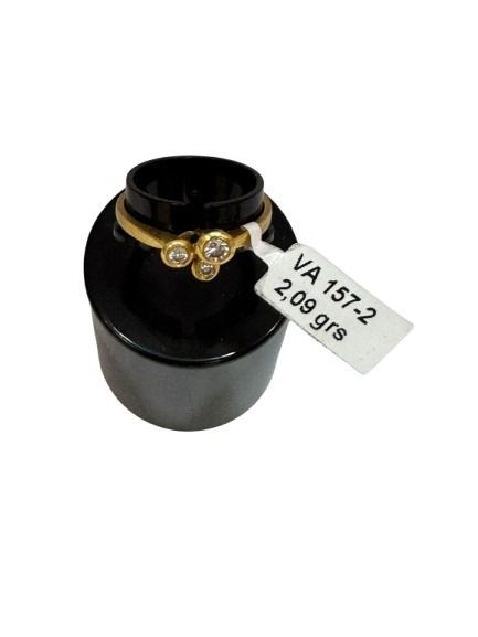 Anillo de oro con tres diamantes en expositor negro; etiqueta con precio adjunta.