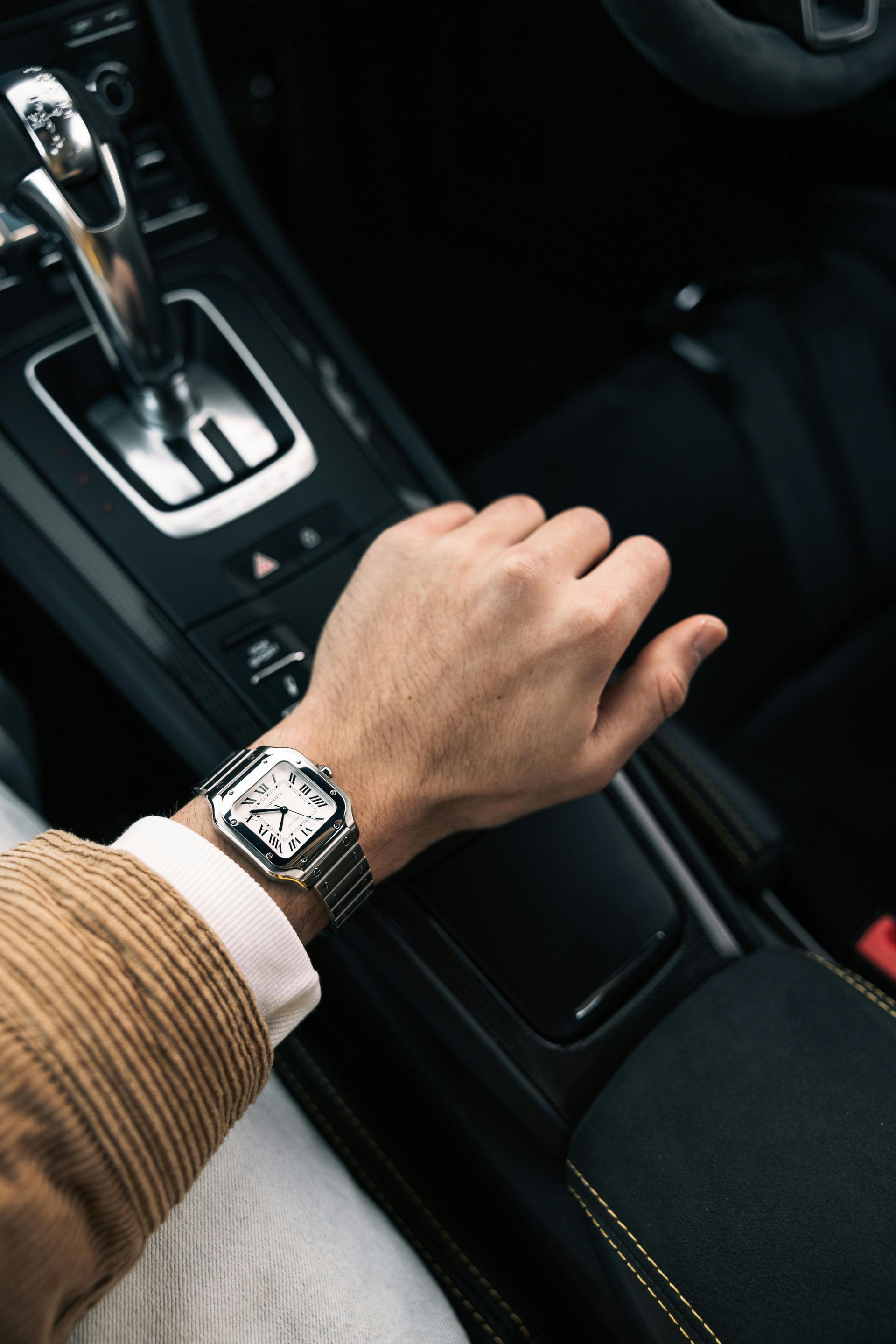 Persona sentada en una mesa con auriculares, teléfono, café, revista y reloj, vistiendo un blazer de rayas.