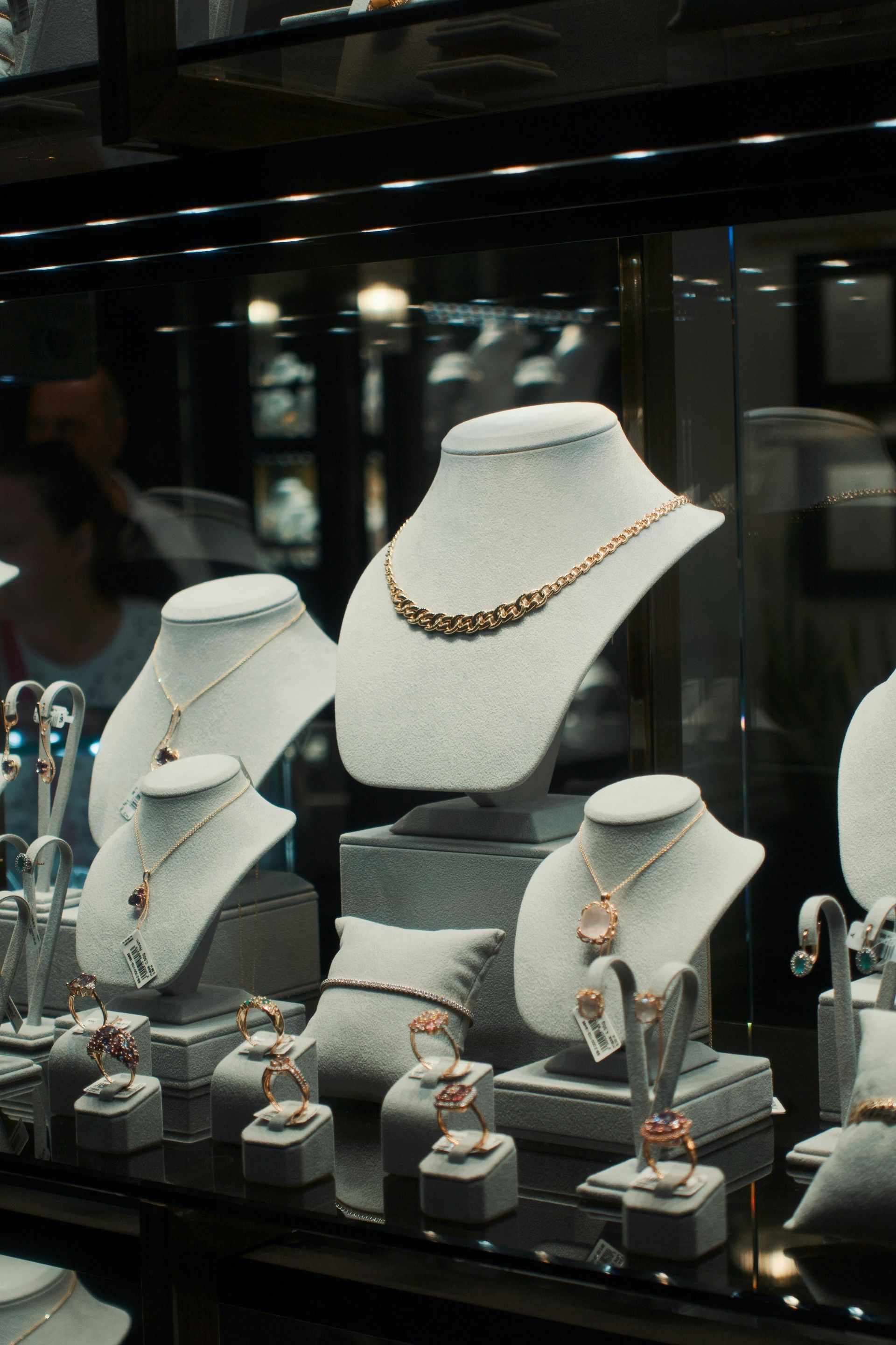 Vitrina de joyería con collares, pulseras y anillos sobre bustos y soportes de maniquí; tonos dorados.