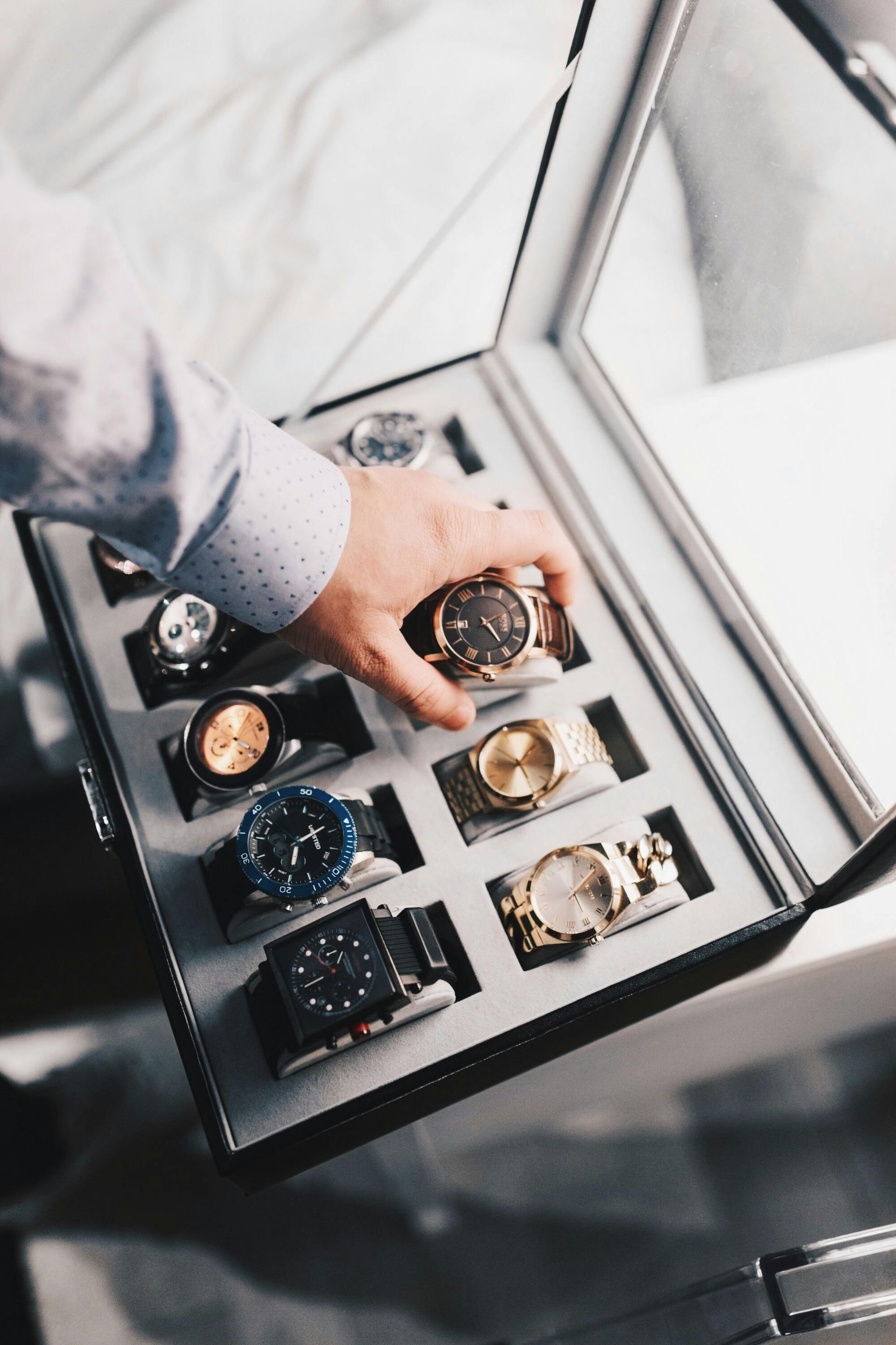 La mano de un hombre seleccionando un reloj de una vitrina llena de diversos relojes de lujo.