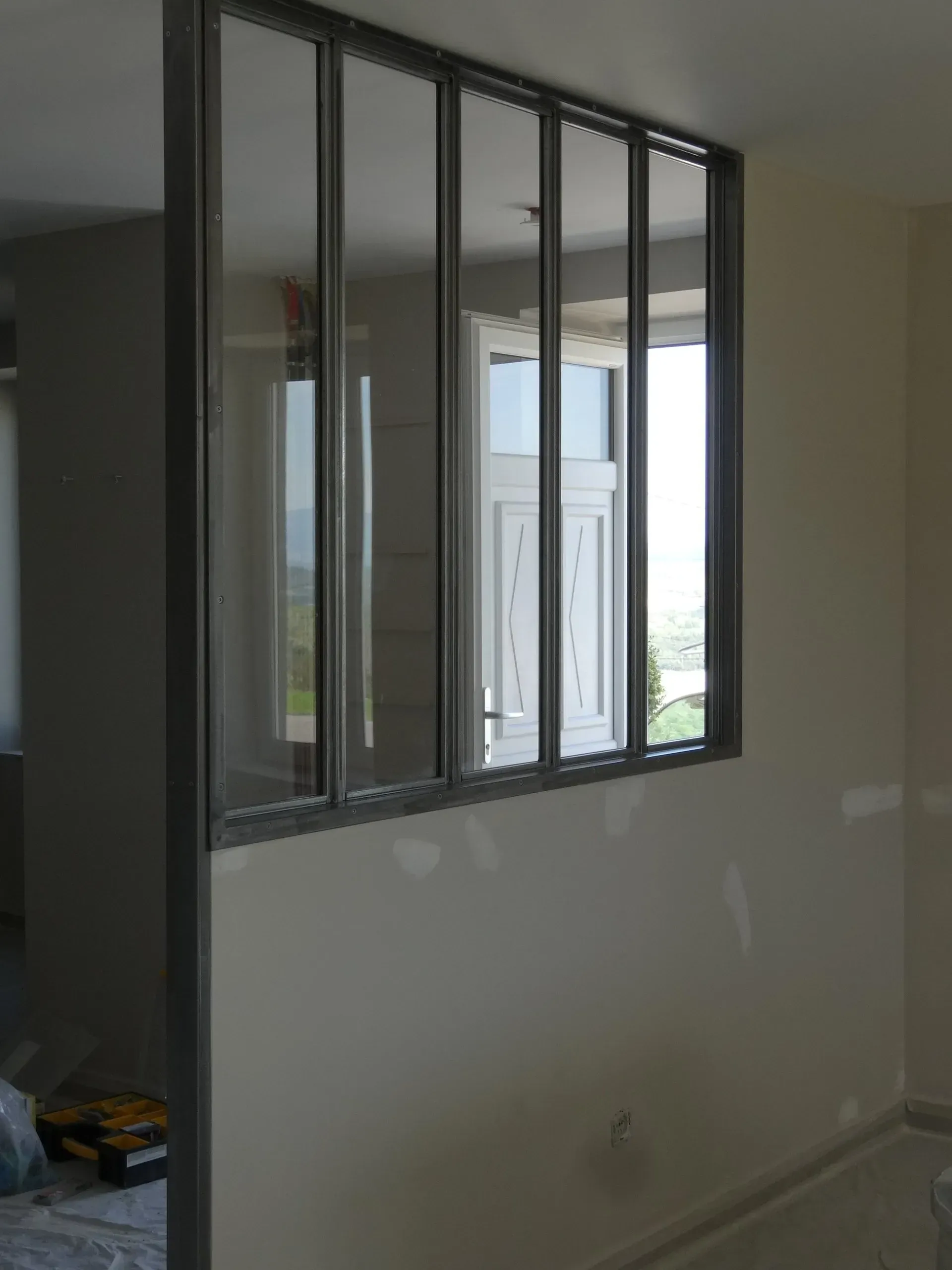 Cloison vitrée avec cadre en métal foncé, séparant deux espaces intérieurs.