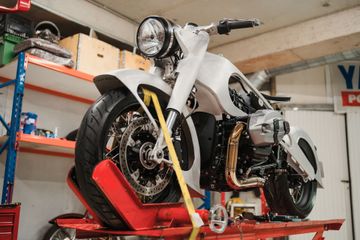 Une moto customisée sur un pont élévateur rouge dans un atelier, avec une carrosserie argentée et une grande roue avant.