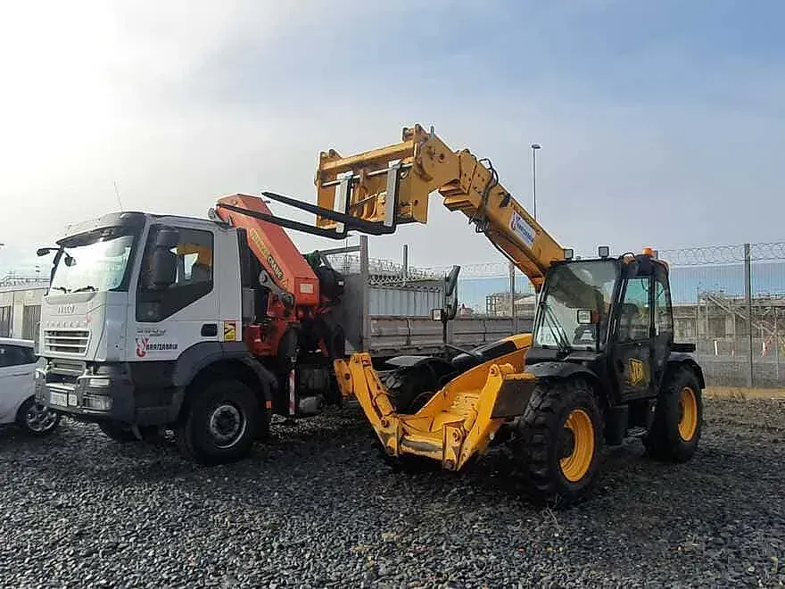 Un camión con una grúa acoplada está aparcado al lado de una carretilla elevadora.