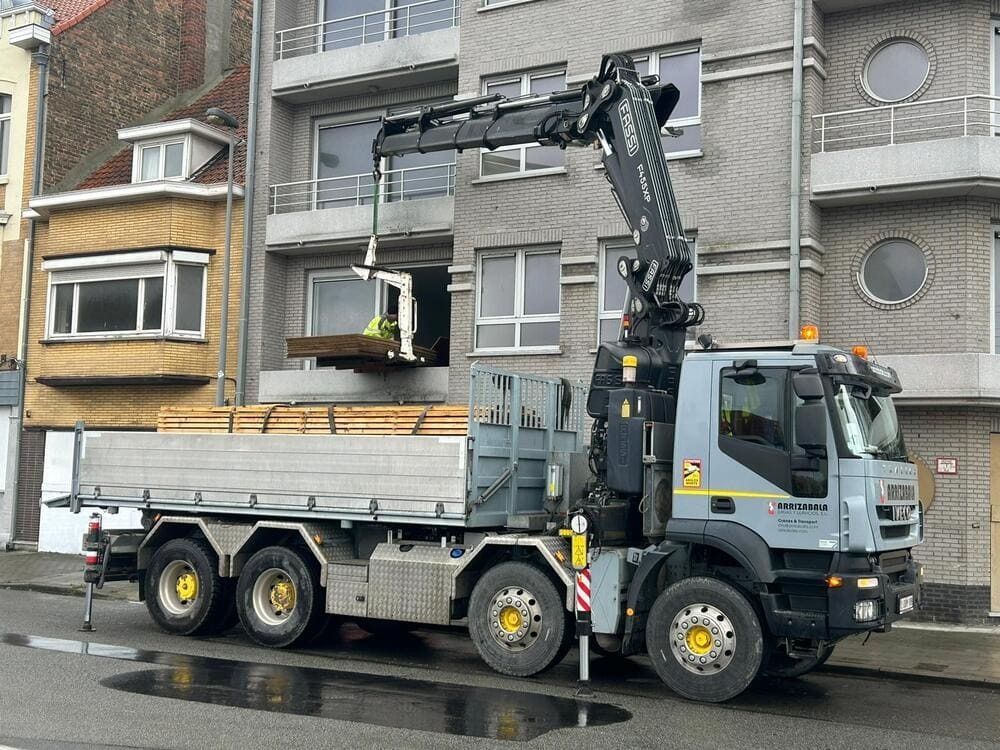 Un camión con una grúa acoplada está estacionado delante de un edificio.