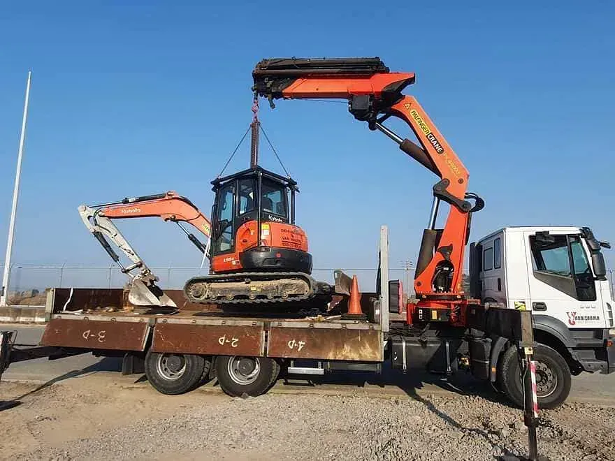 Una grúa está levantando una pequeña excavadora encima de un camión.