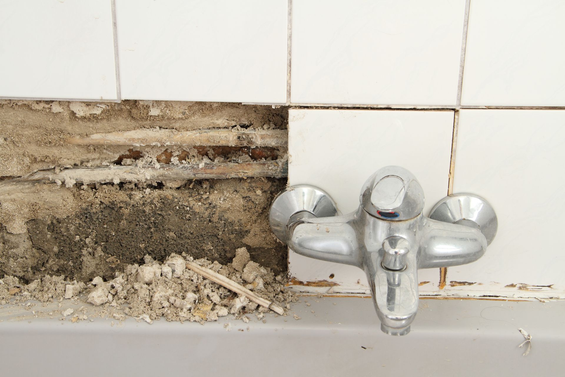 Ein Techniker mit Kappe, blauem Hemd und Arbeitsoverall kniet, um Sanitärrohre in einer Wandverkleidung zu installieren.