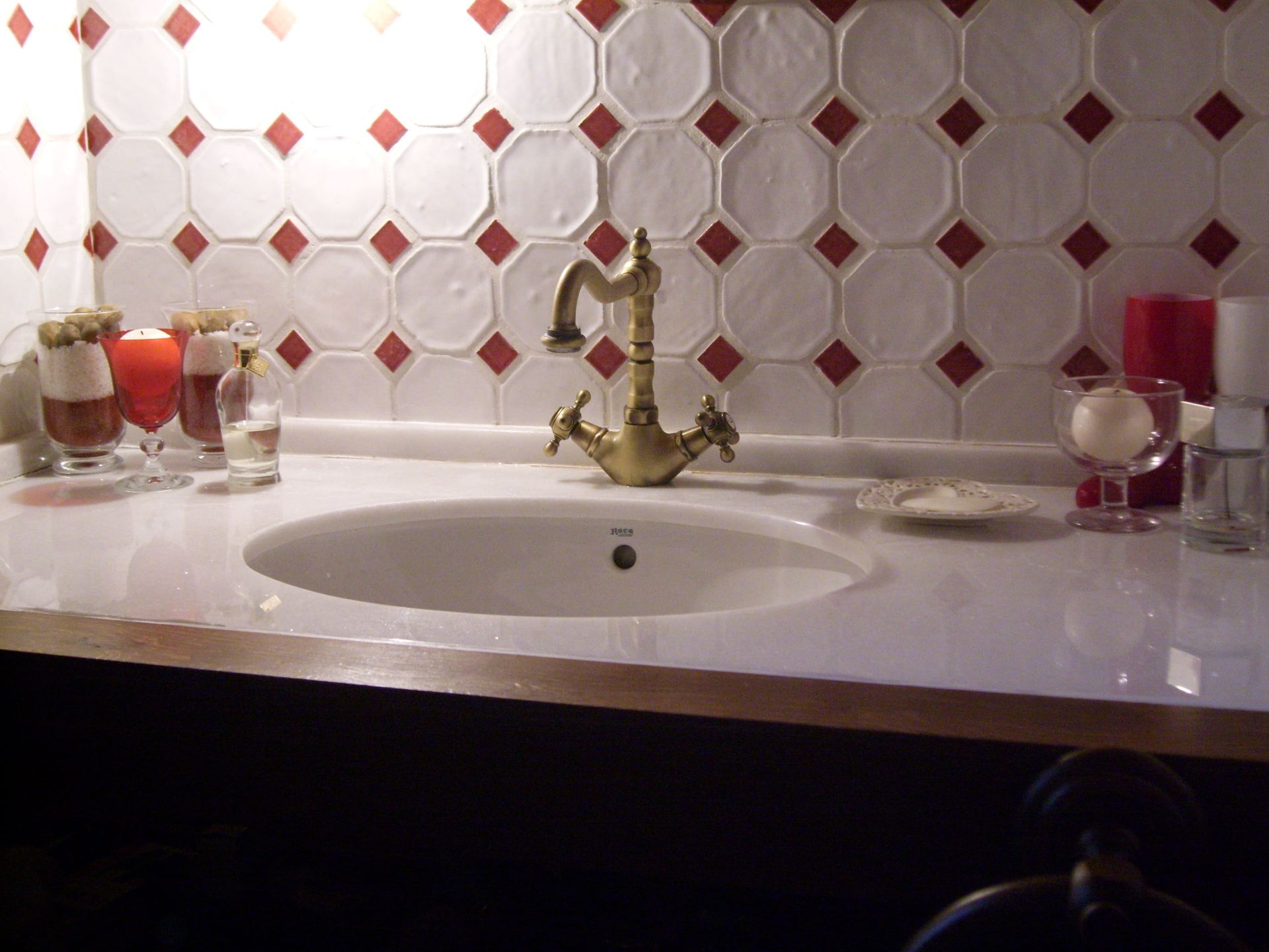 Un lavabo blanco con un grifo de latón colocado sobre una encimera blanca delante de azulejos con dibujos en rojo y blanco.