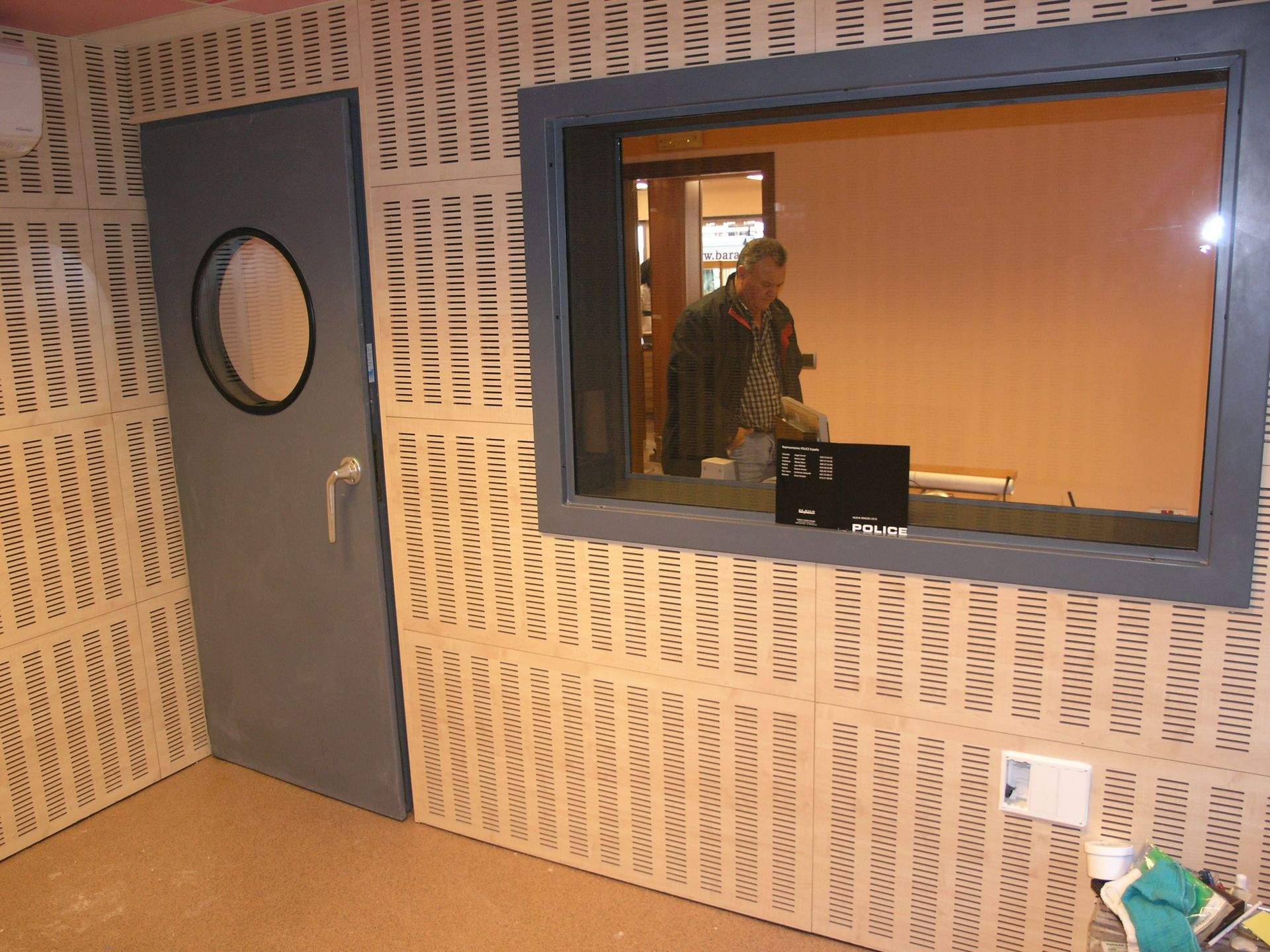 Una habitación insonorizada con paredes texturizadas, una puerta gris con un ojo de buey y una ventana que da a una persona.