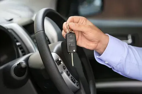 Mano sosteniendo la llave del coche cerca del volante dentro de un coche.