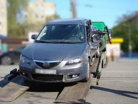 Automóvil gris dañado en una grúa, probablemente después de un accidente, al aire libre en un día soleado.