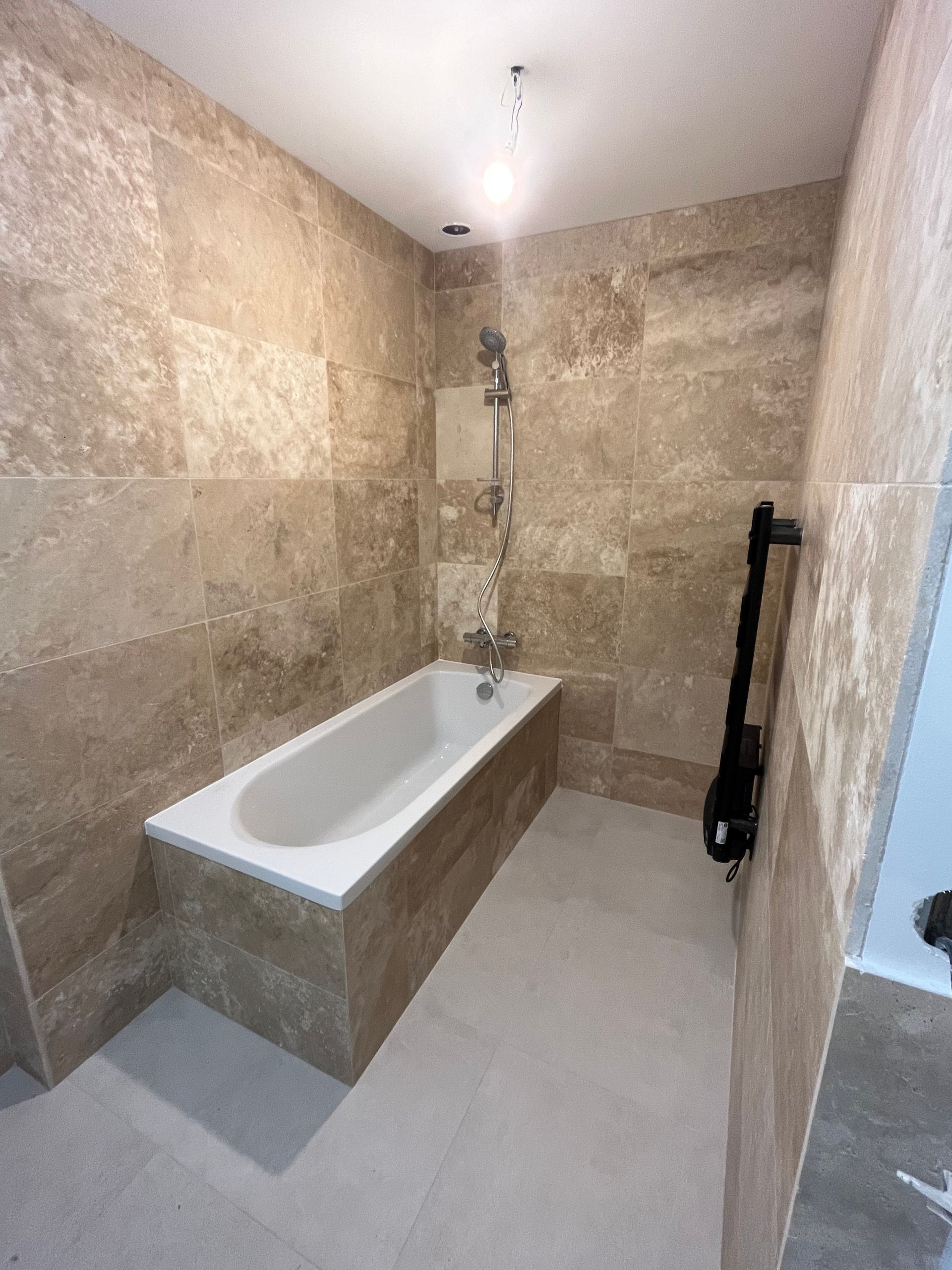 Baignoire avec pommeau de douche dans une salle de bains avec du carrelage marbré et un sèche-serviettes noir