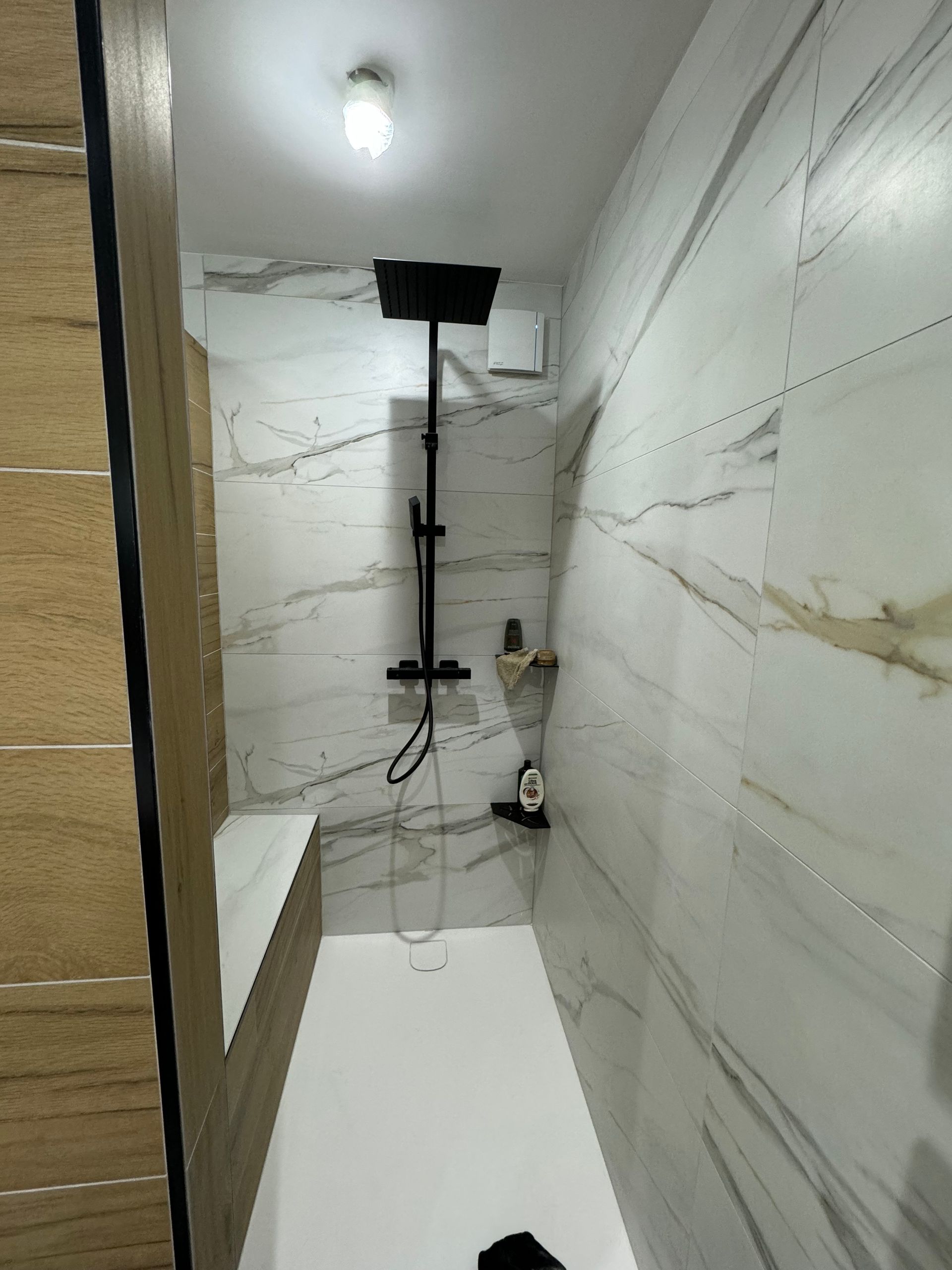 Salle de bains avec une double vasque, des meubles en bois, un sèche-serviettes noir et du carrelage marbré