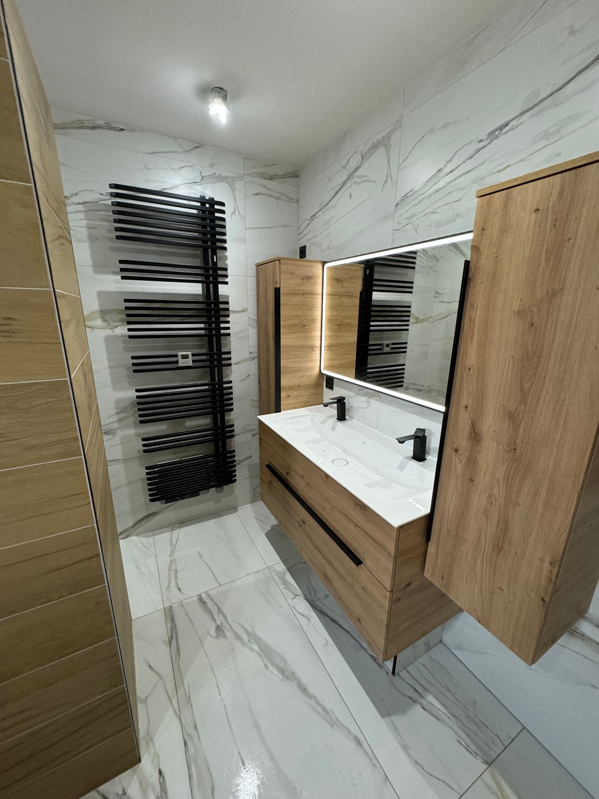 Salle de bains avec une double vasque, des meubles en bois, un sèche-serviettes noir et du carrelage marbré