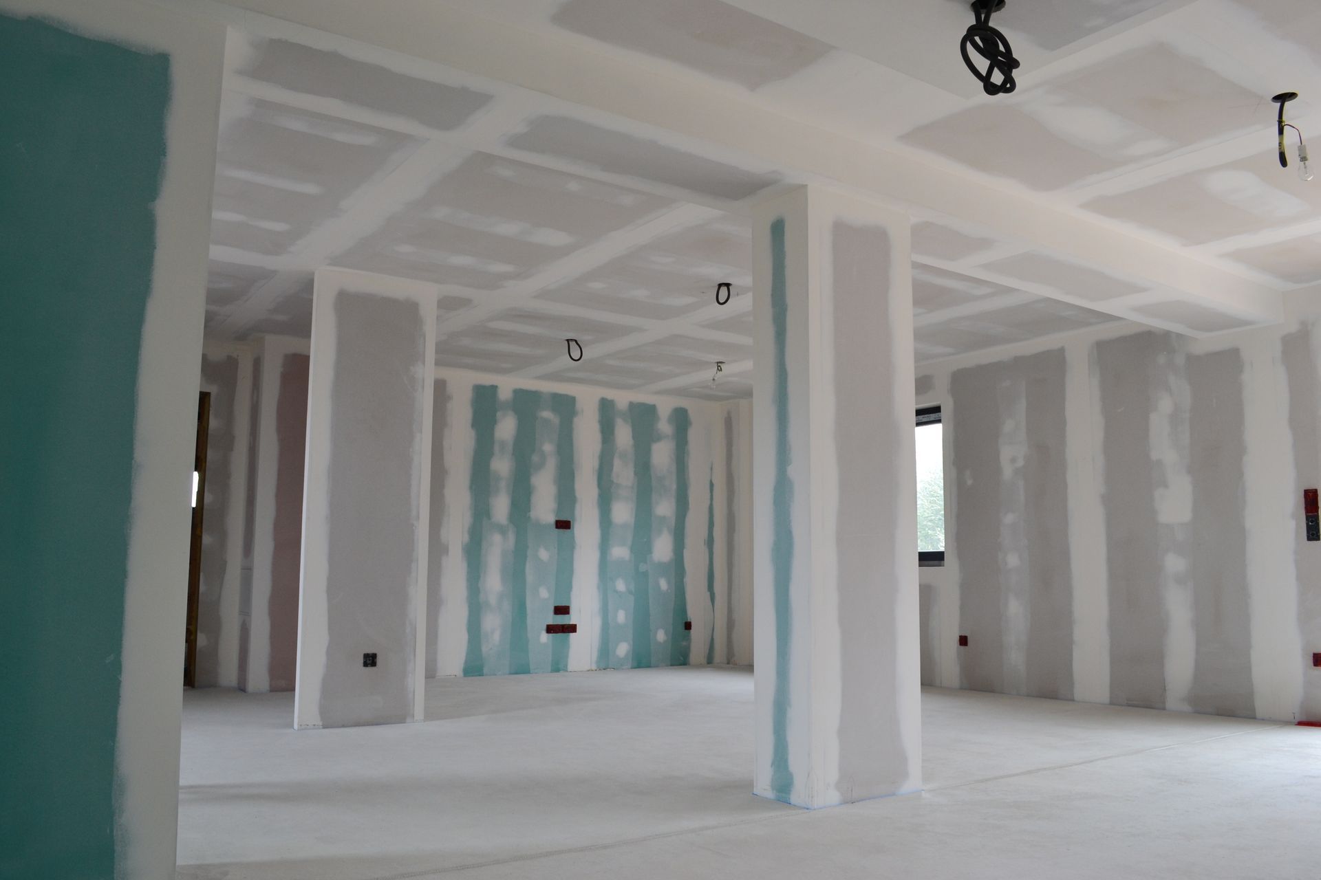 Intérieur d'une pièce en travaux avec murs et plafond en plaques de plâtre blanches, panneaux décoratifs verts et joints apparents.