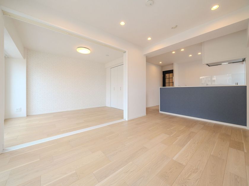 Une pièce à aire ouverte avec un parquet clair, des murs blancs et un îlot de cuisine bleu sous un éclairage encastré.