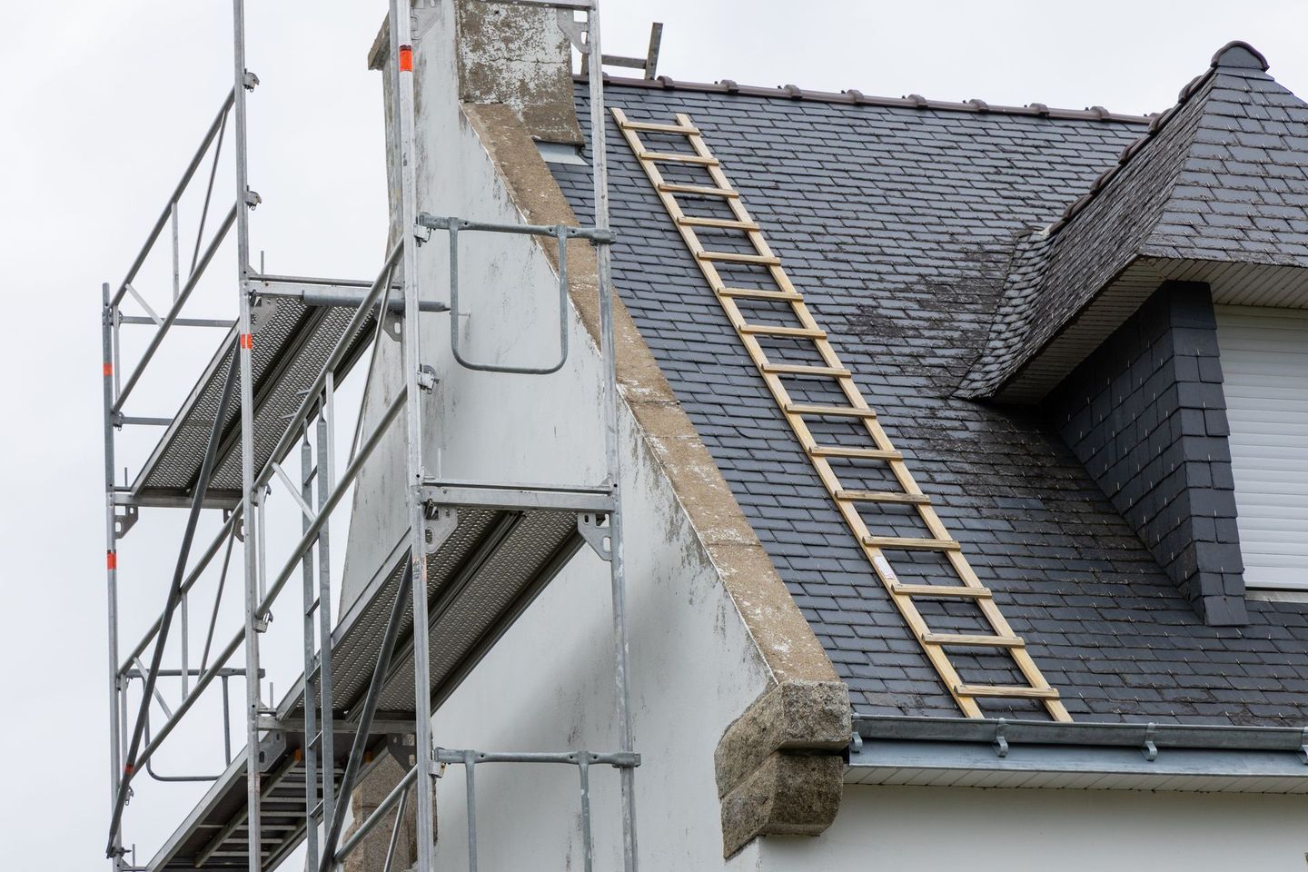 Façade blanche d'une maison en construction, avec des échafaudages installés contre le mur.