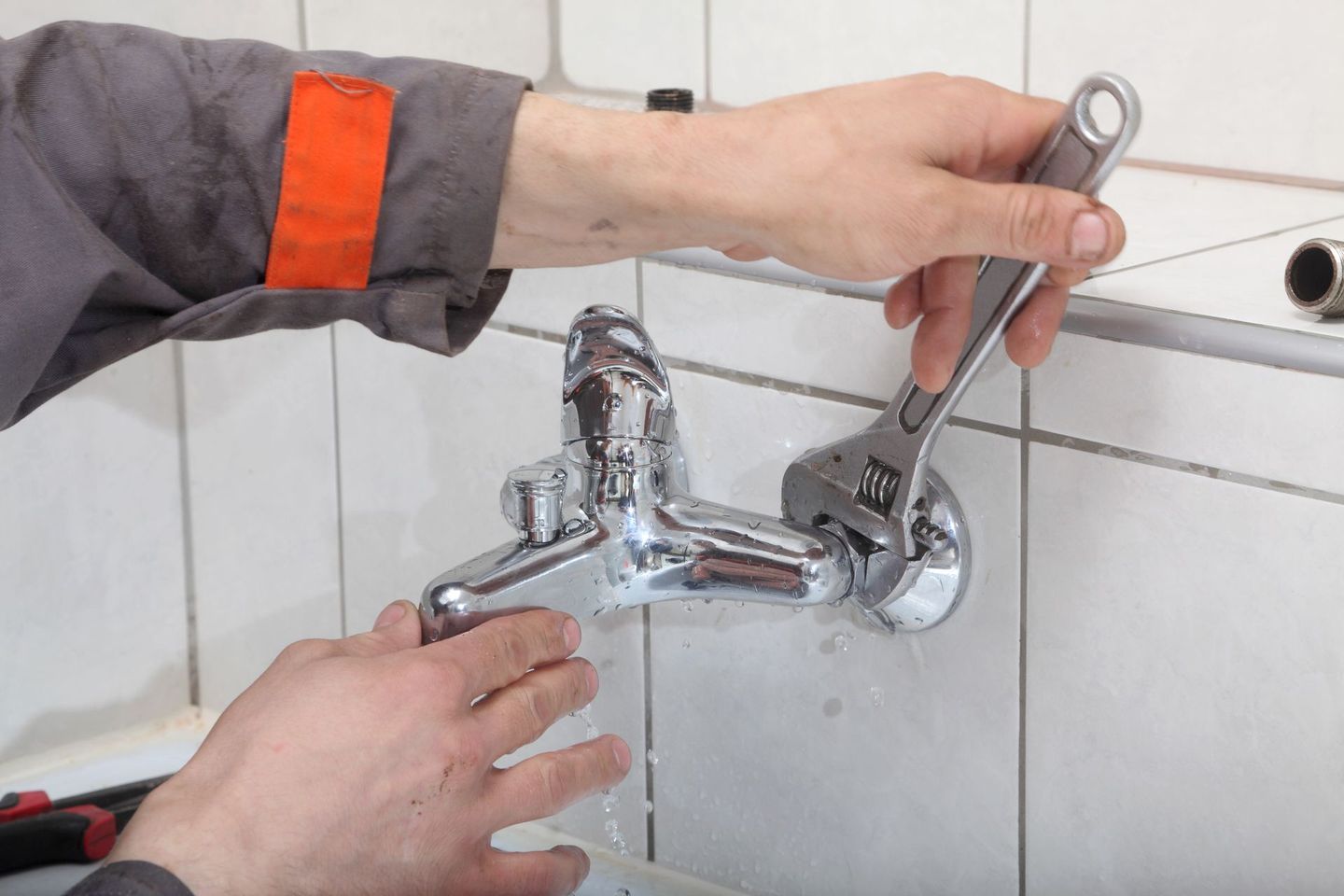 Des mains serrent un robinet chromé dans une salle dde bains carrelée.