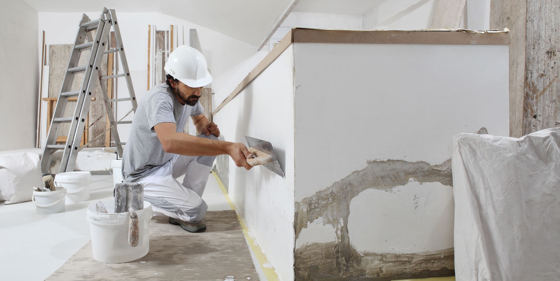 Une personne portant un casque de chantier utilise une truelle métallique pour appliquer du plâtre sur le mur d'une pièce en construction.